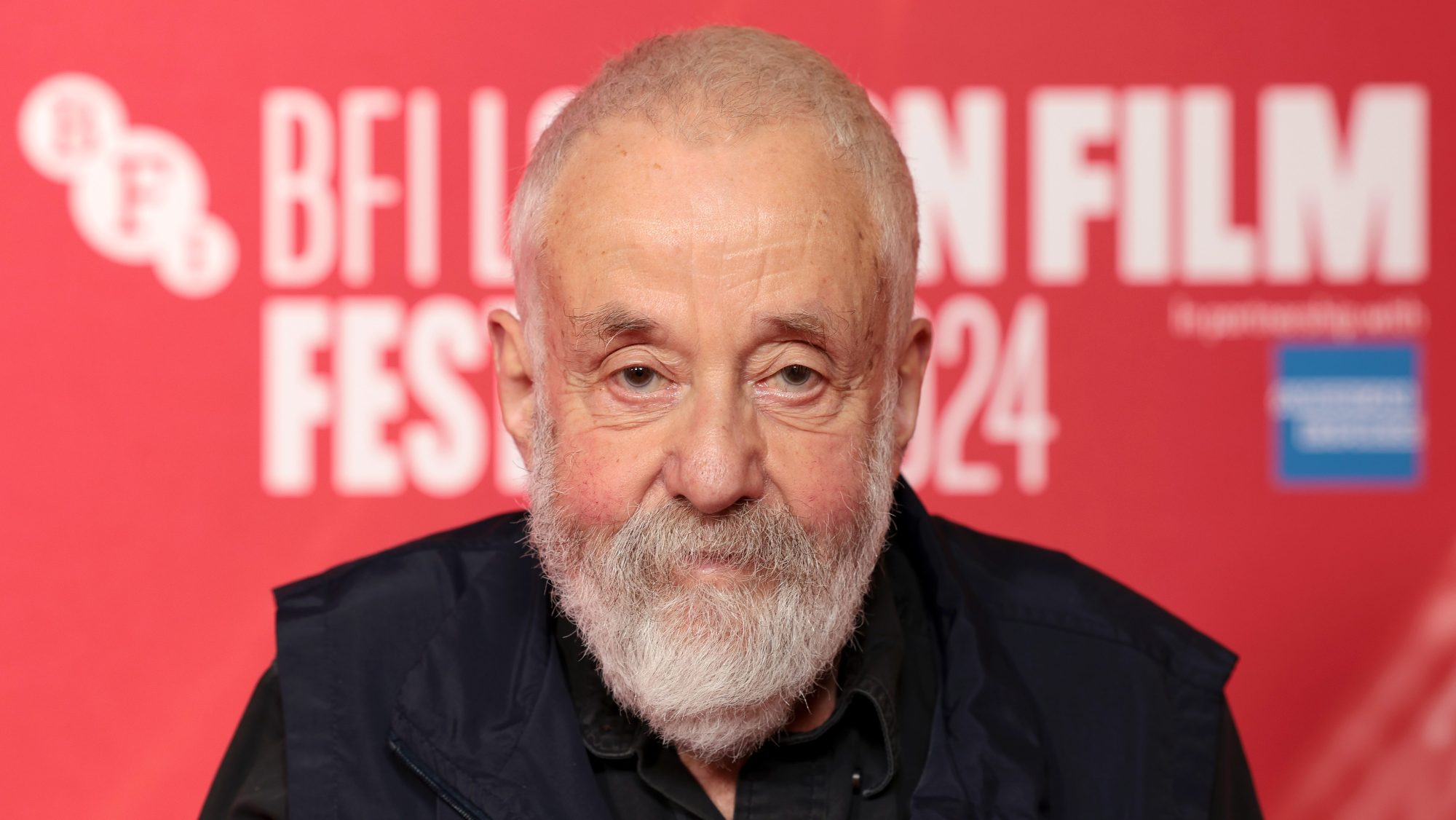 Mike Leigh in front of red backdrop.